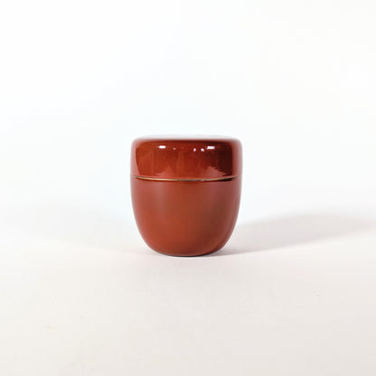 Vue arrière sobre d’un natsume vintage japonais en laque rouge brillante, petite boîte à matcha pour cérémonie du thé