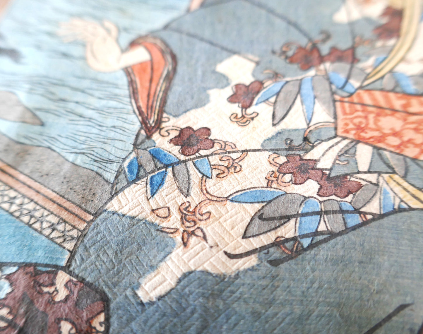 Gros plan sur les motifs floraux du kimono masculin dans l’estampe de Kunisada II, impression fine sur papier texturé.