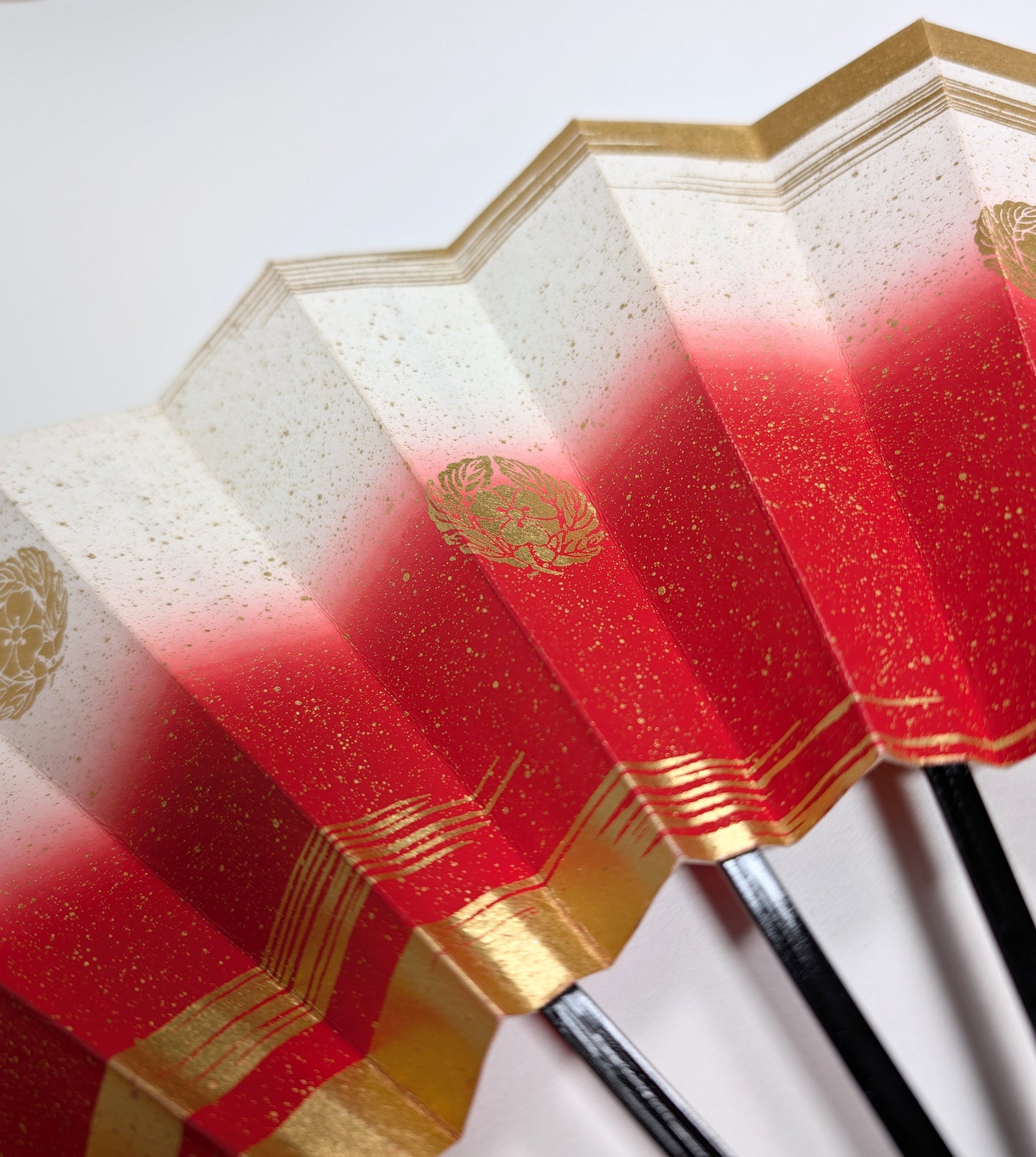 Détail d’un éventail japonais traditionnel en papier cartonné, décoré d’un motif kamon doré et de dégradés rouge et or, emblématique de l’artisanat nippon.