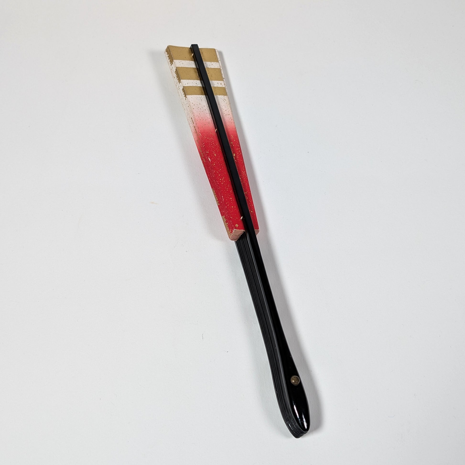Éventail japonais fermé avec manche en bois laqué noir, papier cartonné rouge et or, accessoire traditionnel de cérémonie ou de danse.