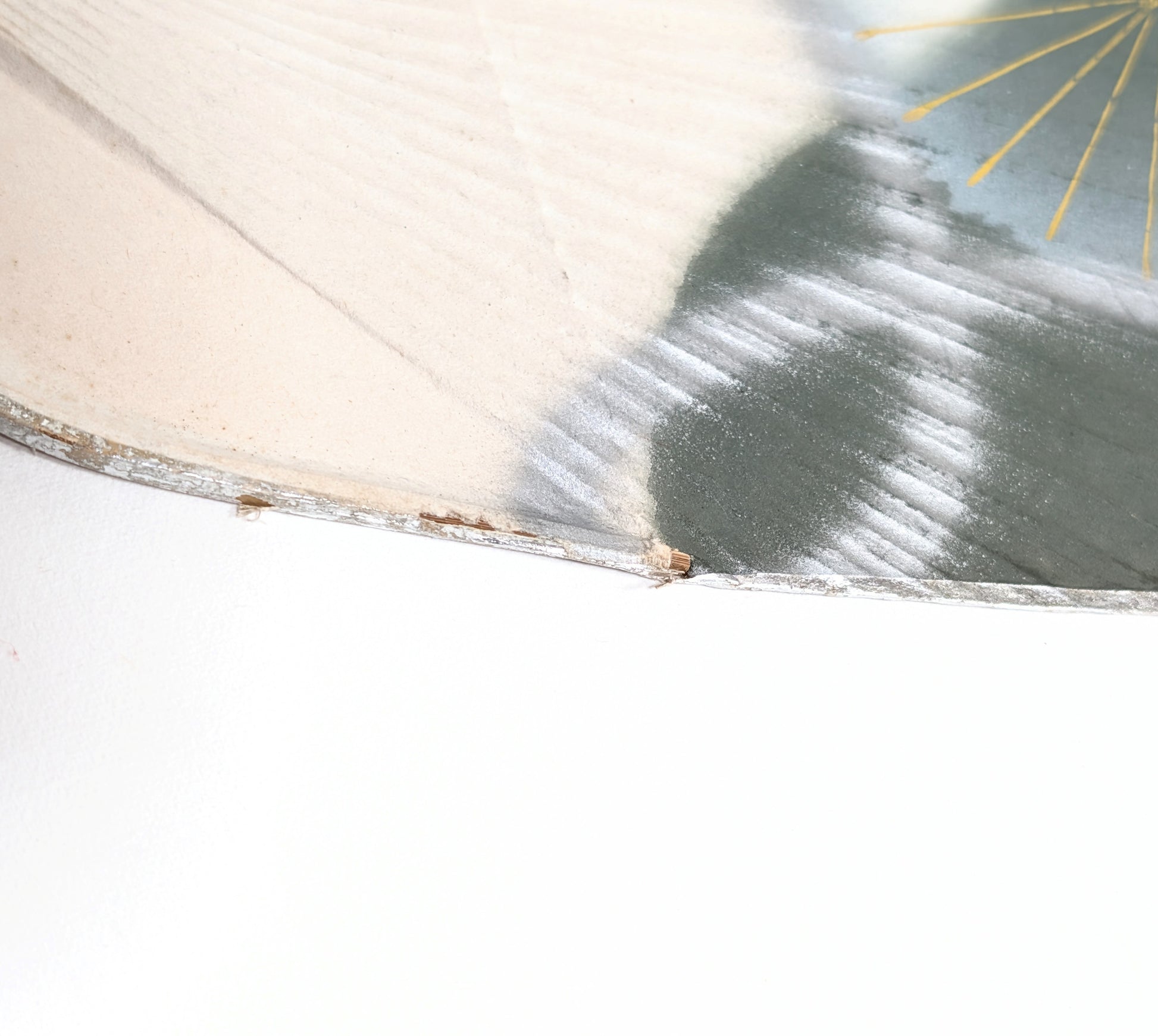 Détail de la bordure argentée et des marques du temps sur un éventail japonais rigide en papier.