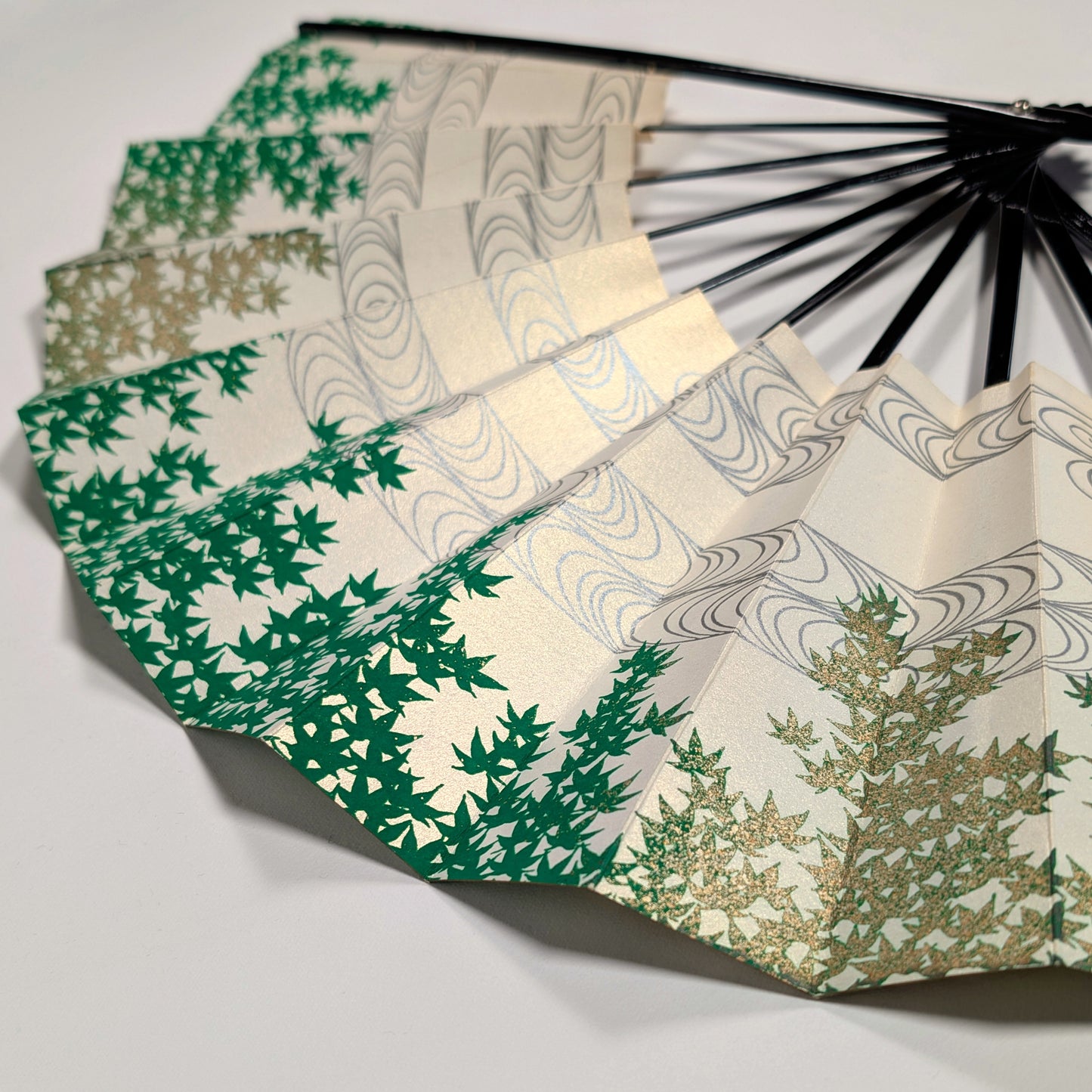Vue rapprochée d’un éventail japonais vert, ivoire et or pâle à motif d’aomomiji et de ryūsui.