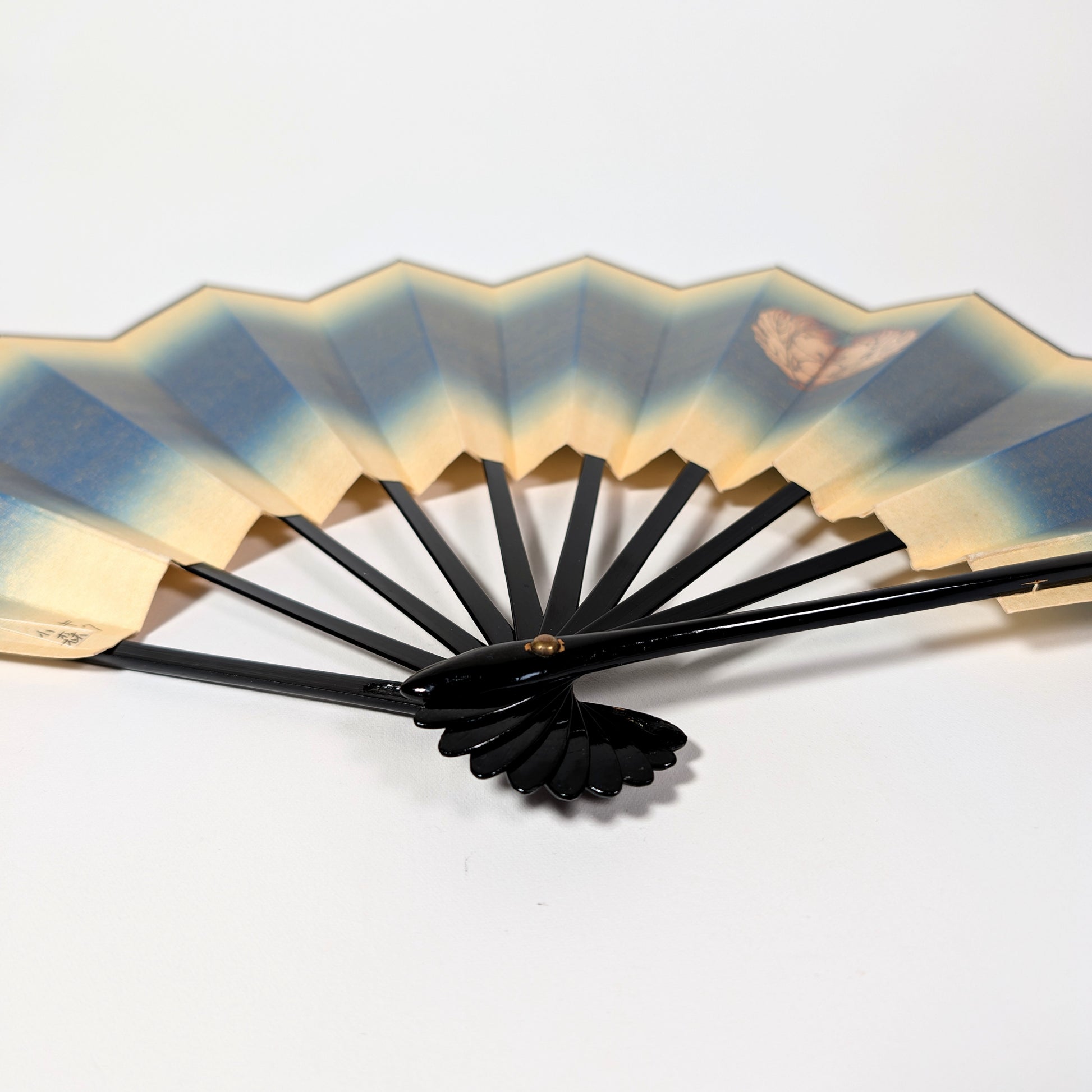 Éventail japonais vintage ouvert avec kamon floral, monture noire laquée et décor irisé bleu et doré.