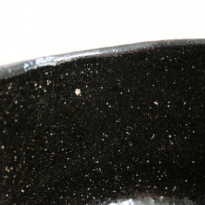 Glaçure noire mouchetée à l’intérieur du matchawan, avec fines inclusions claires et reflets profonds du kuro-raku.
