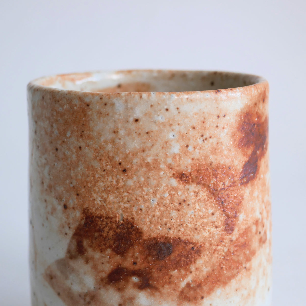 Gros plan de la glaçure Shino d'une tasse japonaise, surface piquetée yuzu-hada et nuances blanc crème et brun rouille.