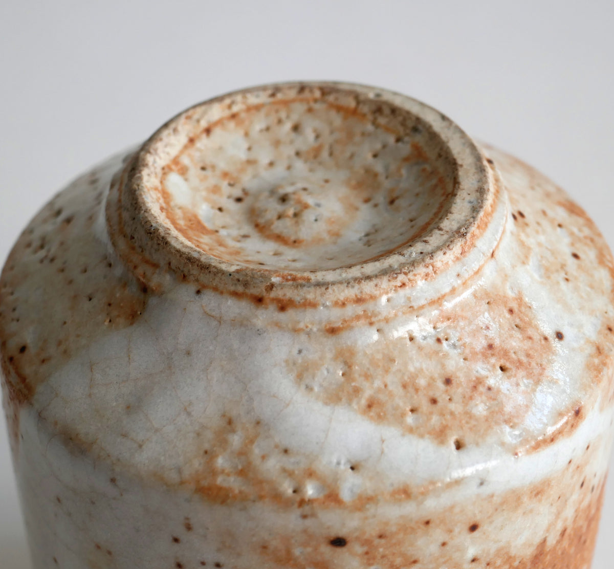 Détail du pied tournassé d'une tasse à thé japonaise Shino, avec anneaux concentriques et glaçure crème orangée.
