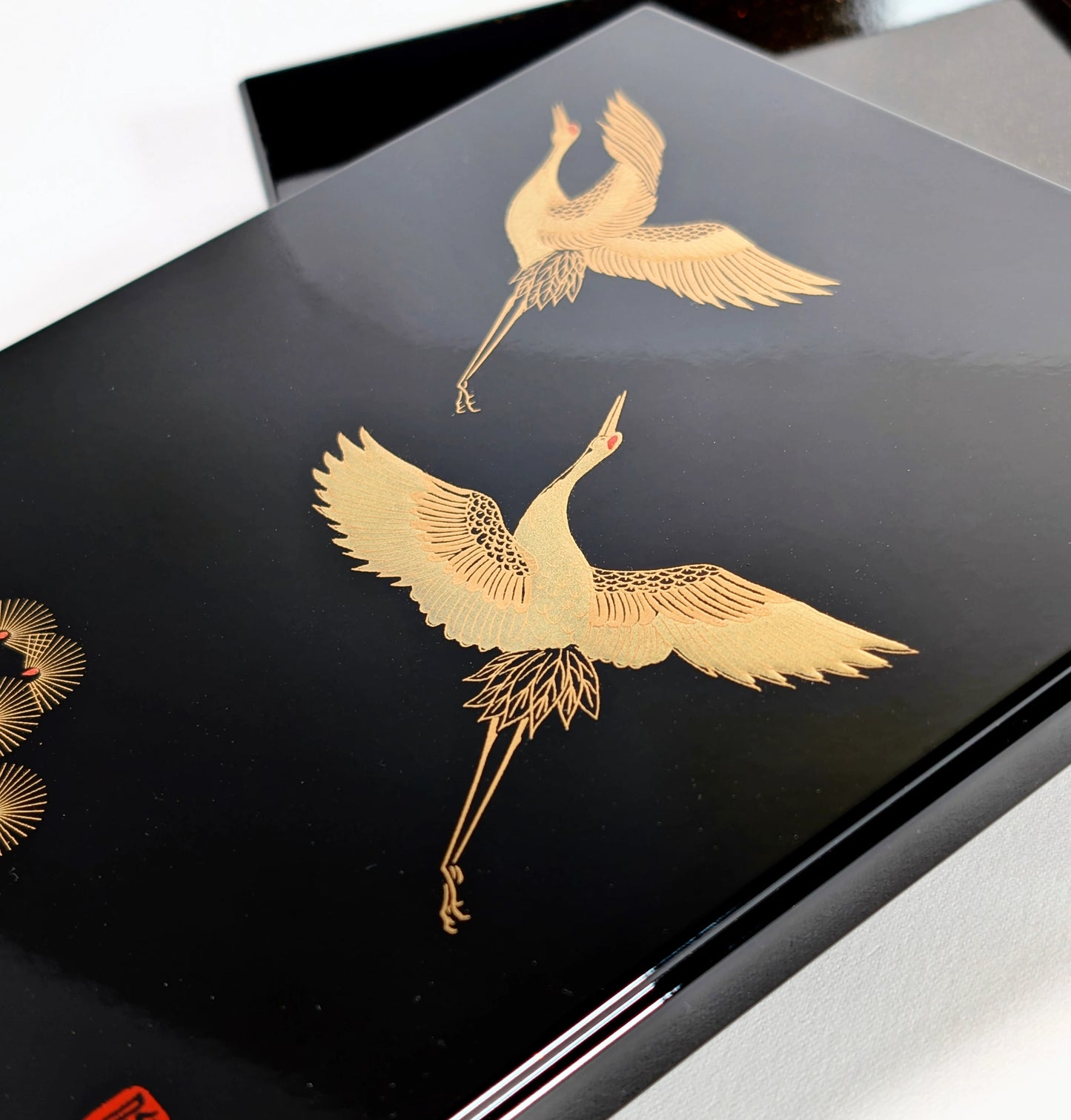 Gros plan sur deux grues tsuru dorées en maki-e sur laque urushi noire brillante.