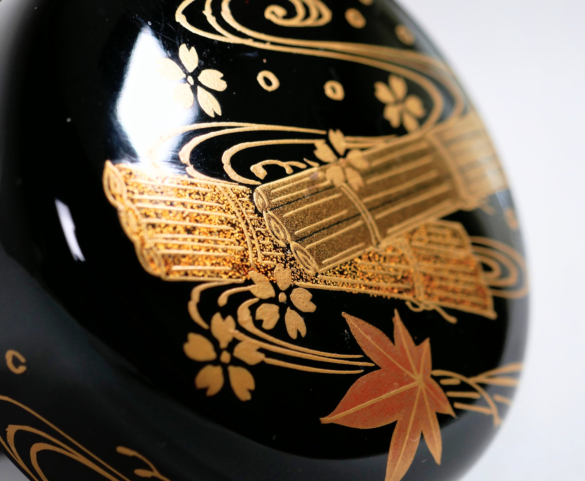Gros plan sur le décor maki-e doré 花筏, poudres d’or et lignes d’eau sur laque urushi noire authentique
