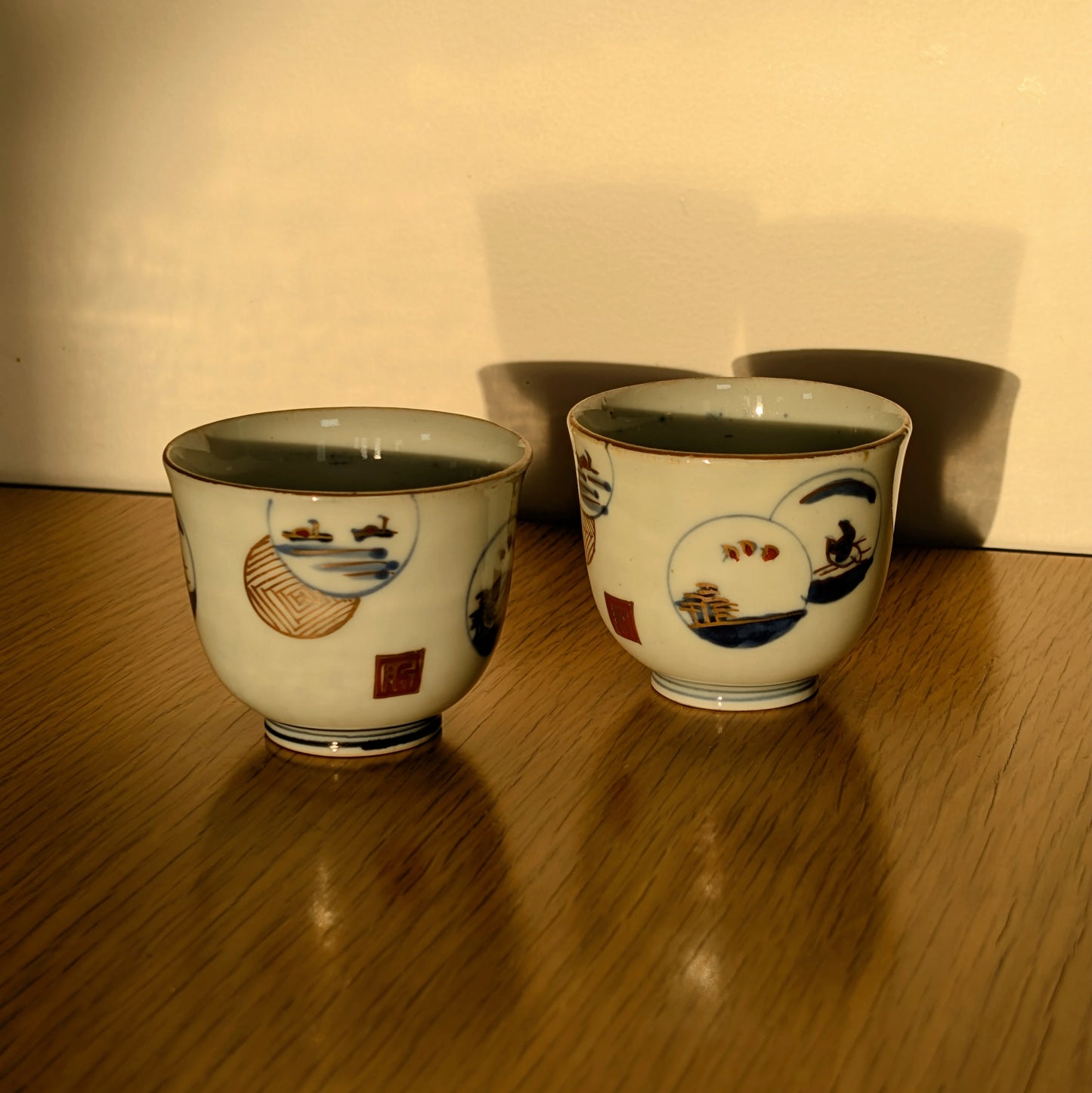 Paire de guinomi à saké en porcelaine Arita Hizen, époque Edo tardif, photographiés en lumière naturelle sur table en bois.