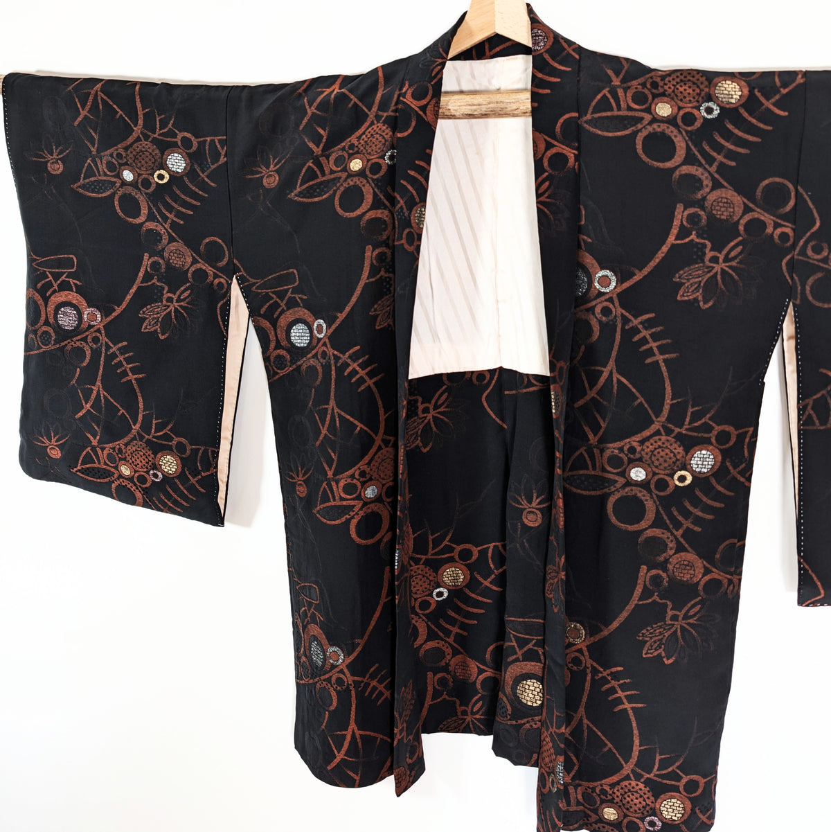 Veste traditionnelle japonaise haori en brocart noir, aux manches larges et décor de fleurs stylisées, arabesques et motifs géométriques cuivrés.