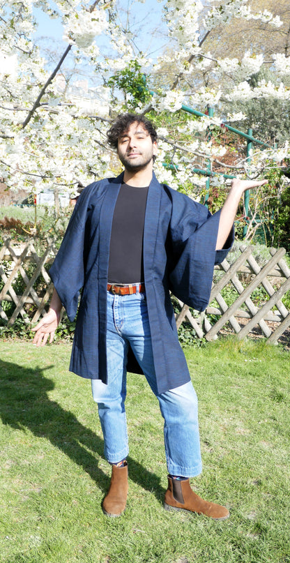 Haori homme porté par Richard, en jean et t-shirt noir, pose décontractée sous les cerisiers en fleurs.