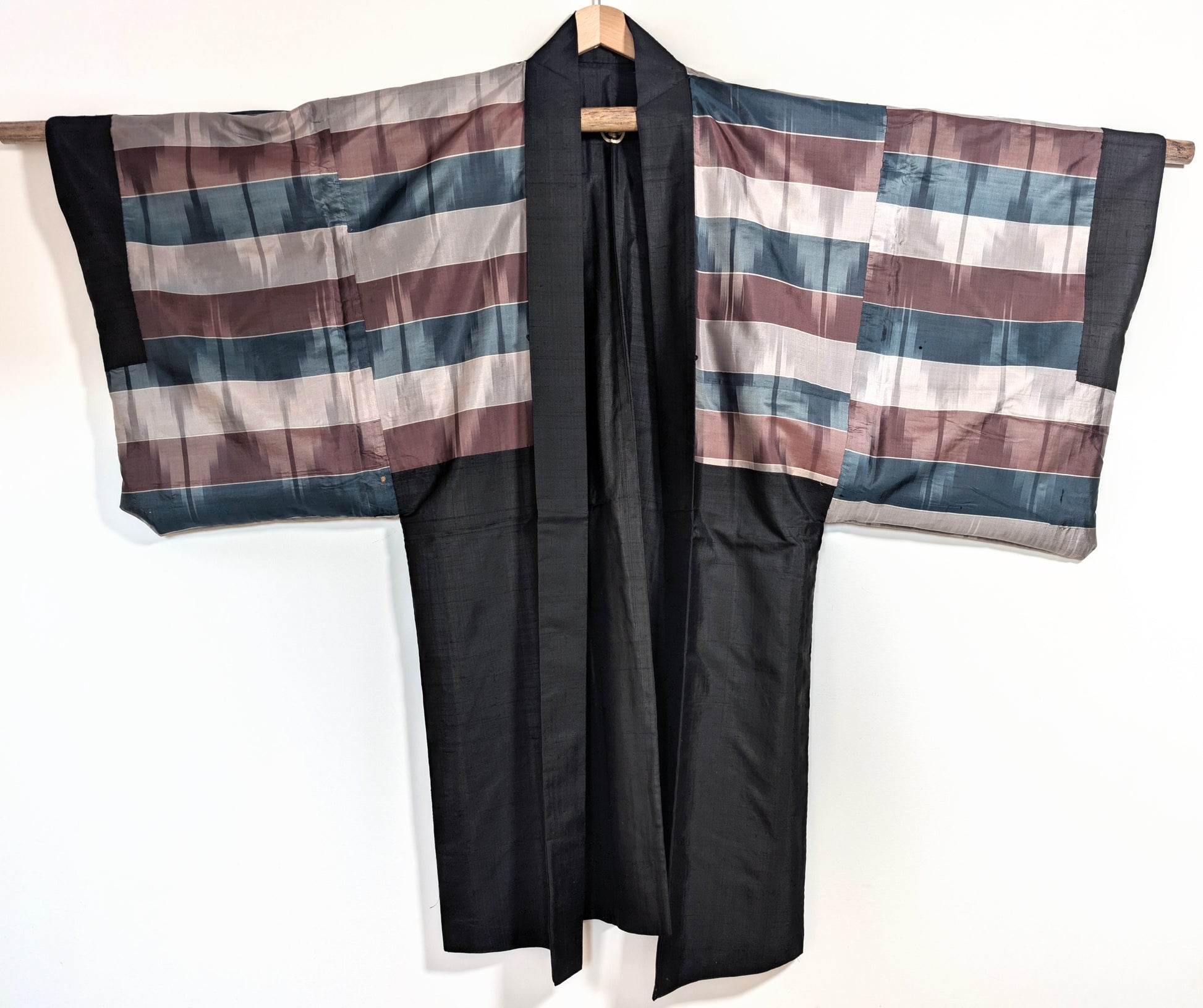 Haori japonais ancien en soie noire ouvert, laissant apparaître la doublure traditionnelle rayée