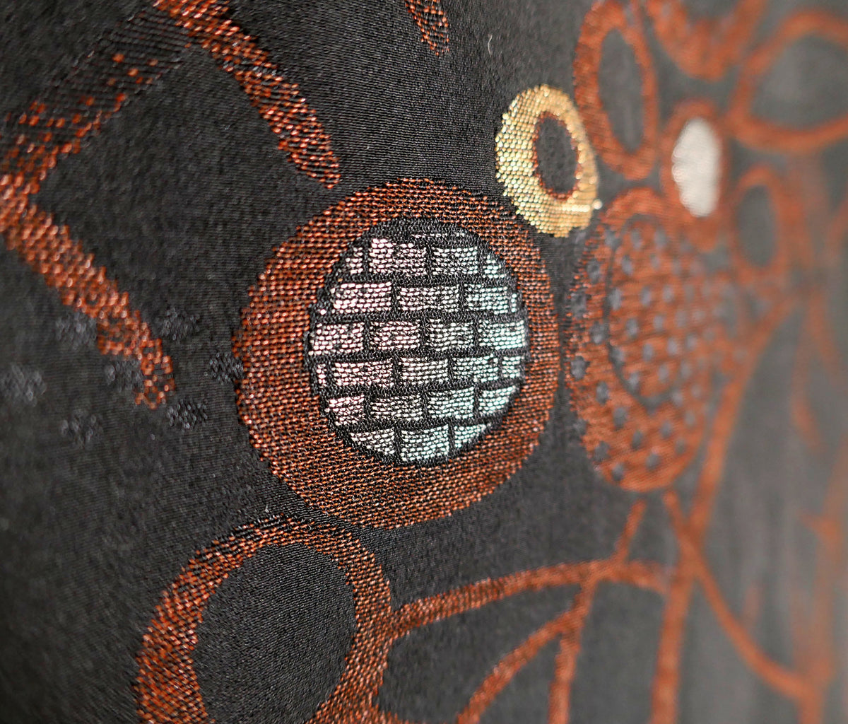 Gros plan sur un motif circulaire argenté entouré de cuivre, révélant les détails du tissage du brocart de soie noire japonais.