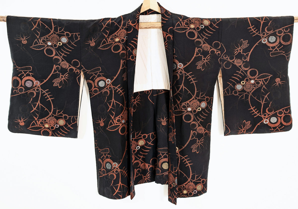 Haori japonais vintage pour femme en soie noire, présenté de face avec ses grandes manches et ses motifs floraux abstraits cuivrés.