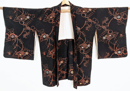Haori japonais vintage pour femme en soie noire, présenté de face avec ses grandes manches et ses motifs floraux abstraits cuivrés.