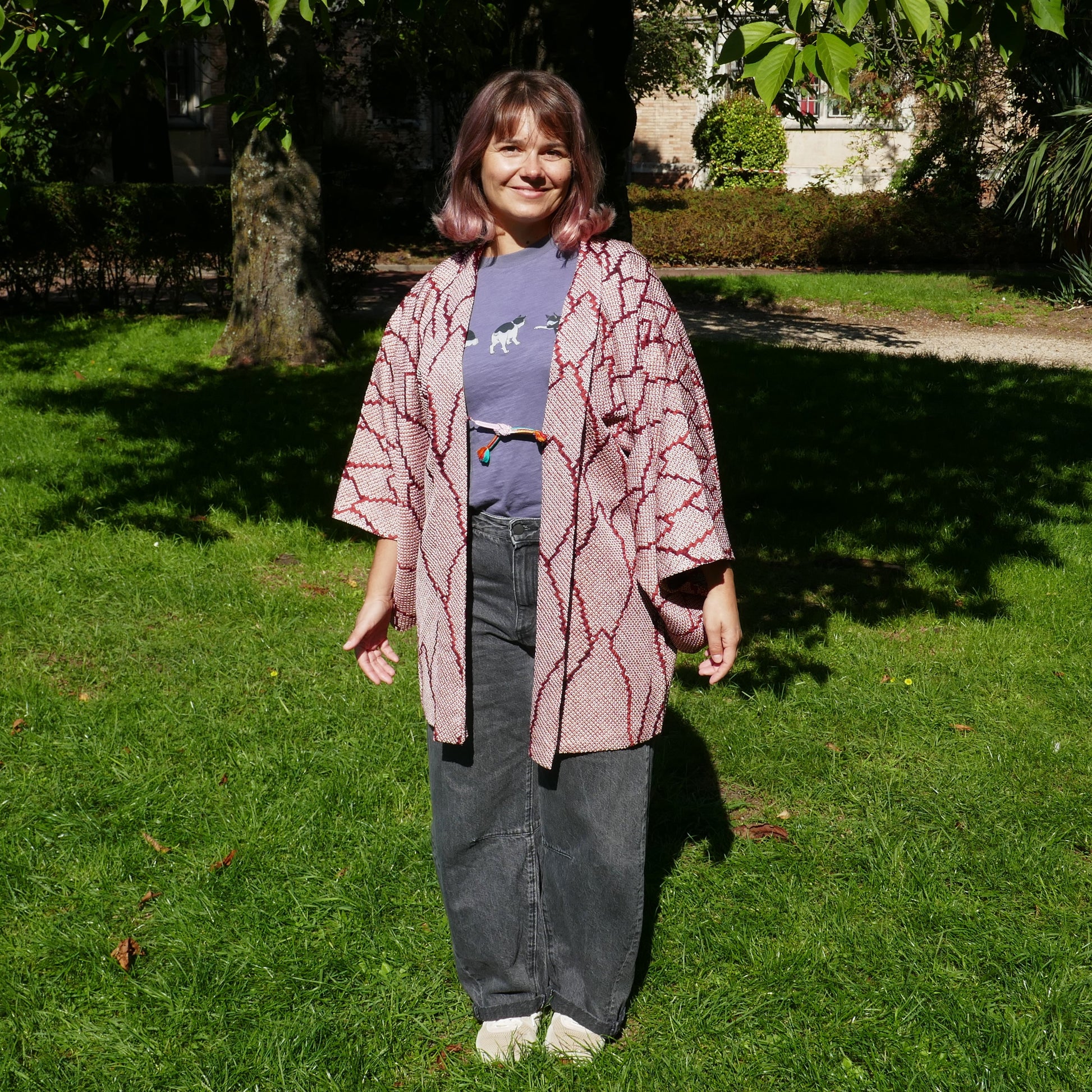 Mikan en veste kimono traditionnelle haori vintage japonais en soie, motif shibori rouge grenat, dans un parc à Paris.