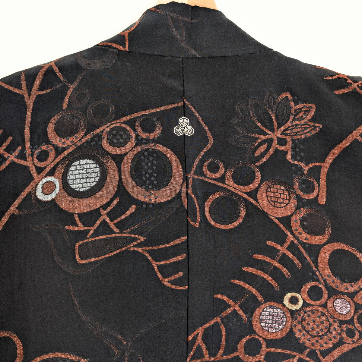 Détail du dos d'un haori japonais en brocart de soie noire, avec arabesques cuivrées, motifs circulaires et petit kamon blanc sous le col.