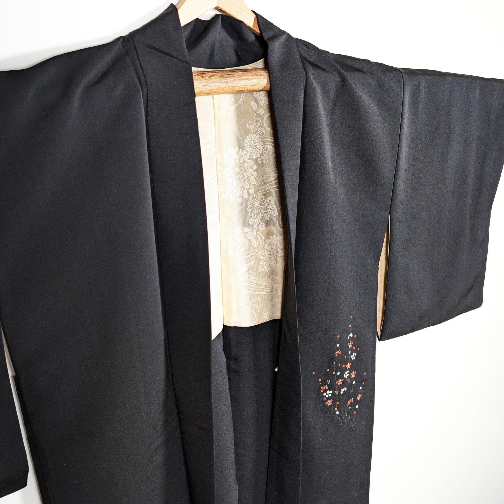 Haori japonais en soie noire habutae, veste kimono élégante avec fleurs de prunier ume rouges, blanches et dorées, doublure ivoire visible.
