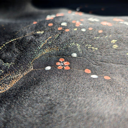 Macro de la soie noire discrètement brillante d’un haori japonais, avec texture rinzu en relief, fleurs ume rouges et blanches et branches dorées.
