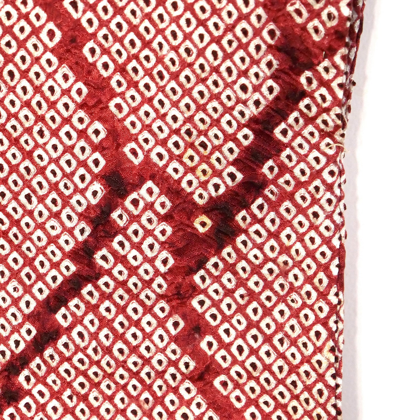 Gros plan du motif shibori couleur grenat sur soie, rendant visible une petite tâche à l'arrière de la manche.
