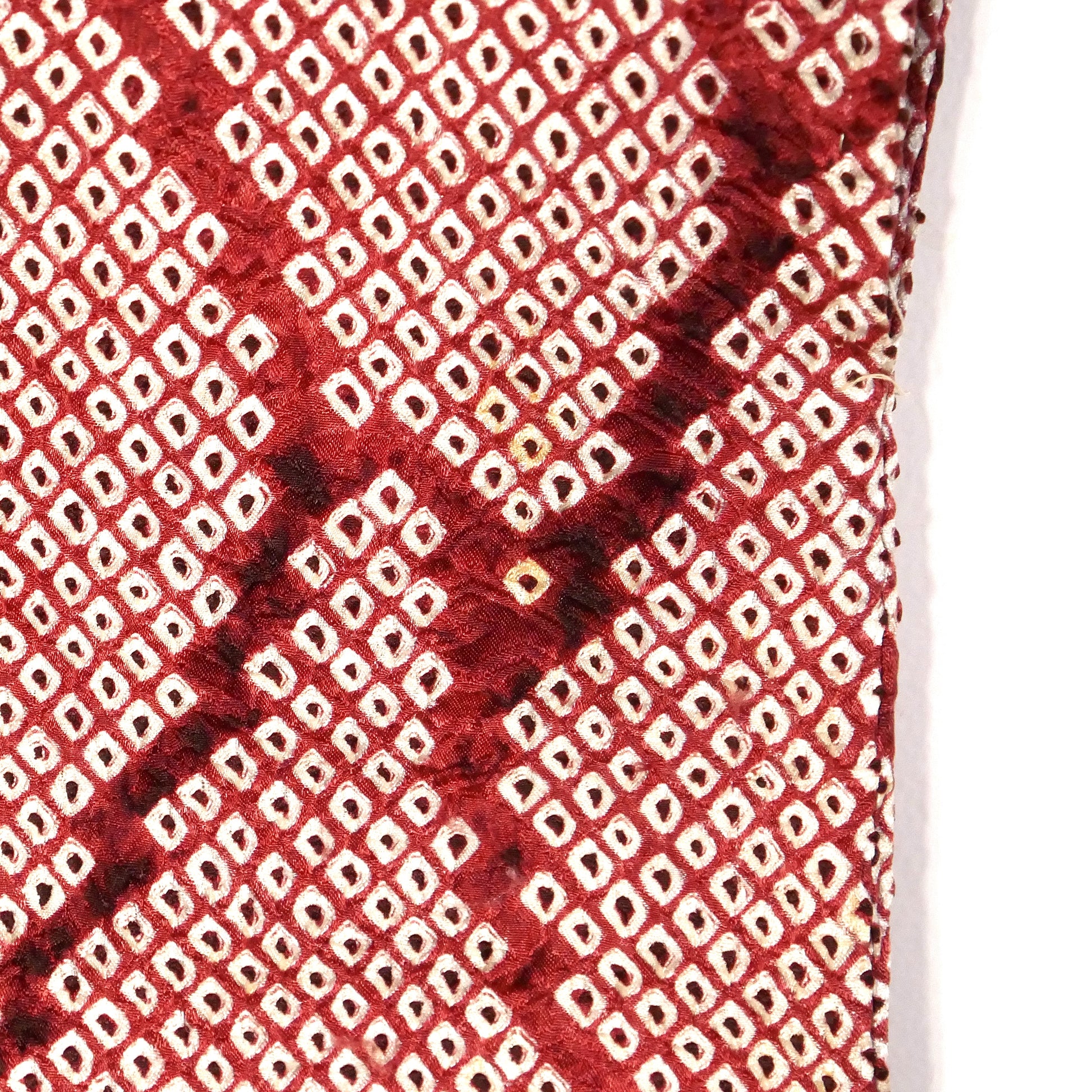 Gros plan du motif shibori couleur grenat sur soie, rendant visible une petite tâche à l'arrière de la manche.