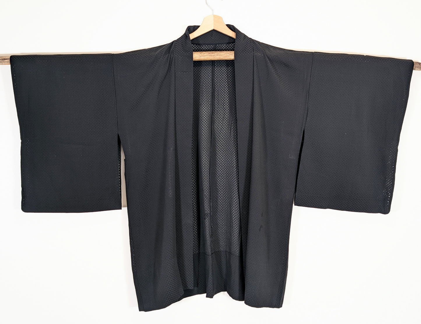 Vue de face d’un haori traditionnel japonais en soie noire monsha, sans doublure, aux manches larges et motif damier ichimatsu.