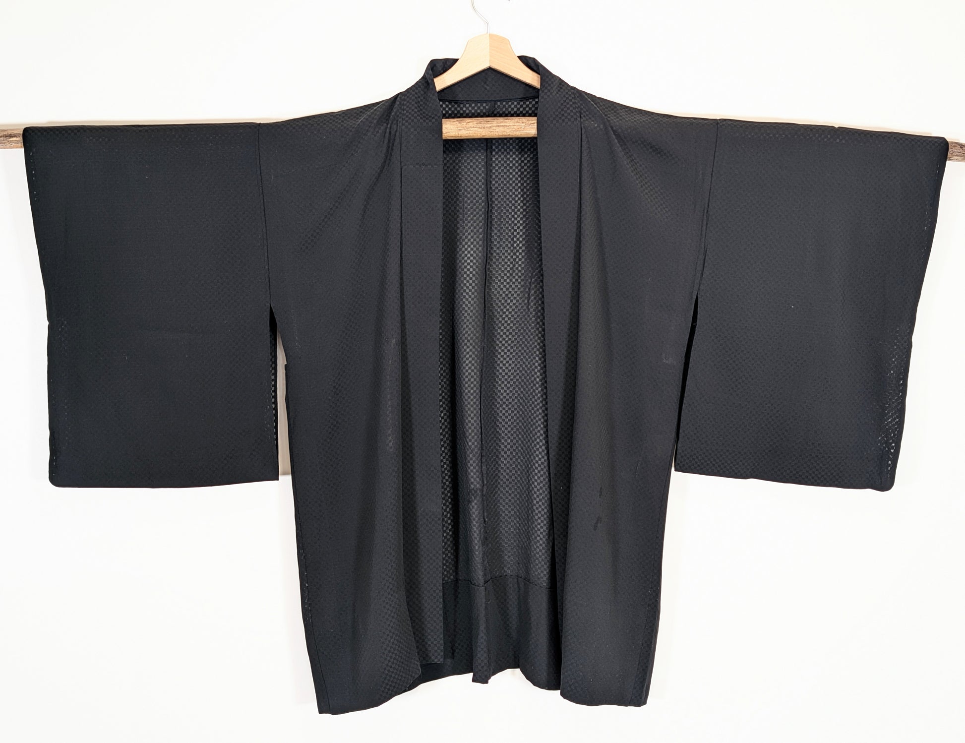 Vue de face d’un haori traditionnel japonais en soie noire monsha, sans doublure, aux manches larges et motif damier ichimatsu.