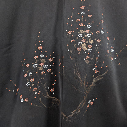 Gros plan du décor dorsal ume sur haori en soie noire, branches de prunier dorées et fleurs rouges blanches au style cérémoniel.