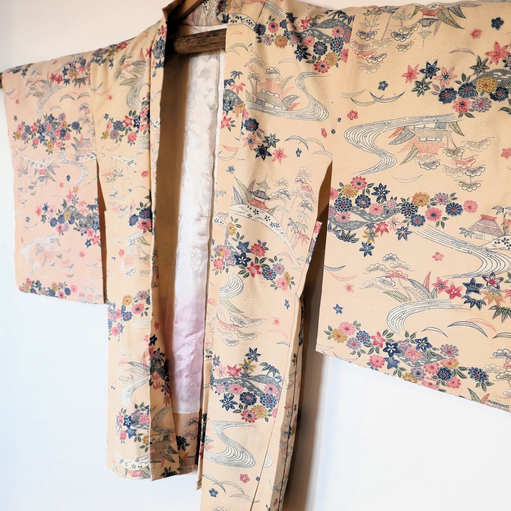 Vue de trois-quarts du haori vintage suspendu, montrant son motif de rivières et fleurs colorées sur fond ivoire