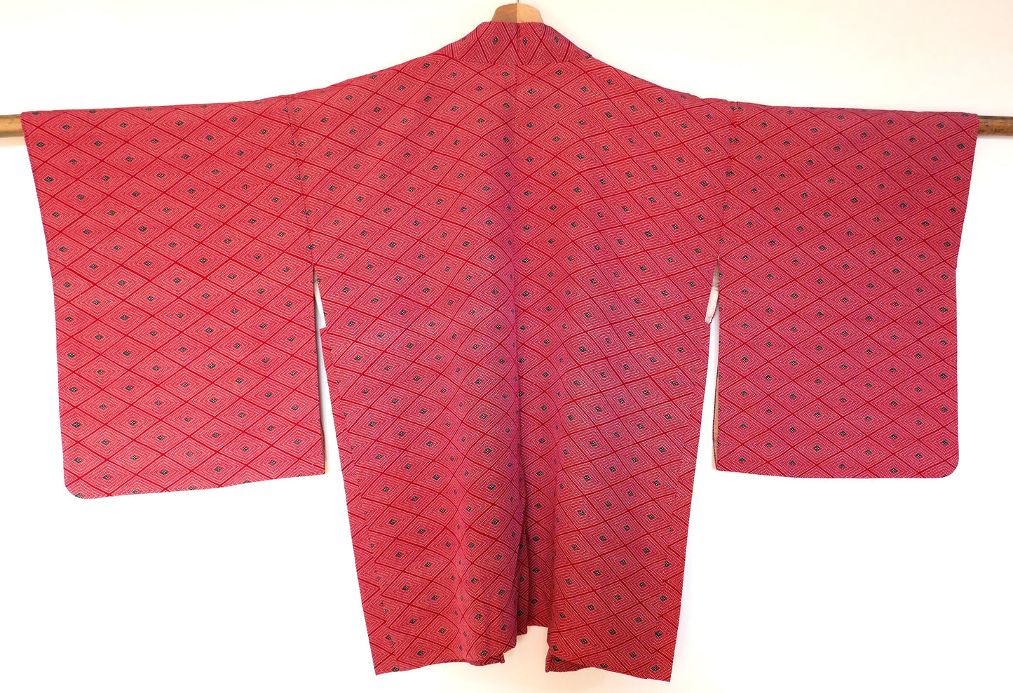  Vue de dos complète d’un haori vintage suspendu, en soie rouge à motifs géométriques losange (菱形).