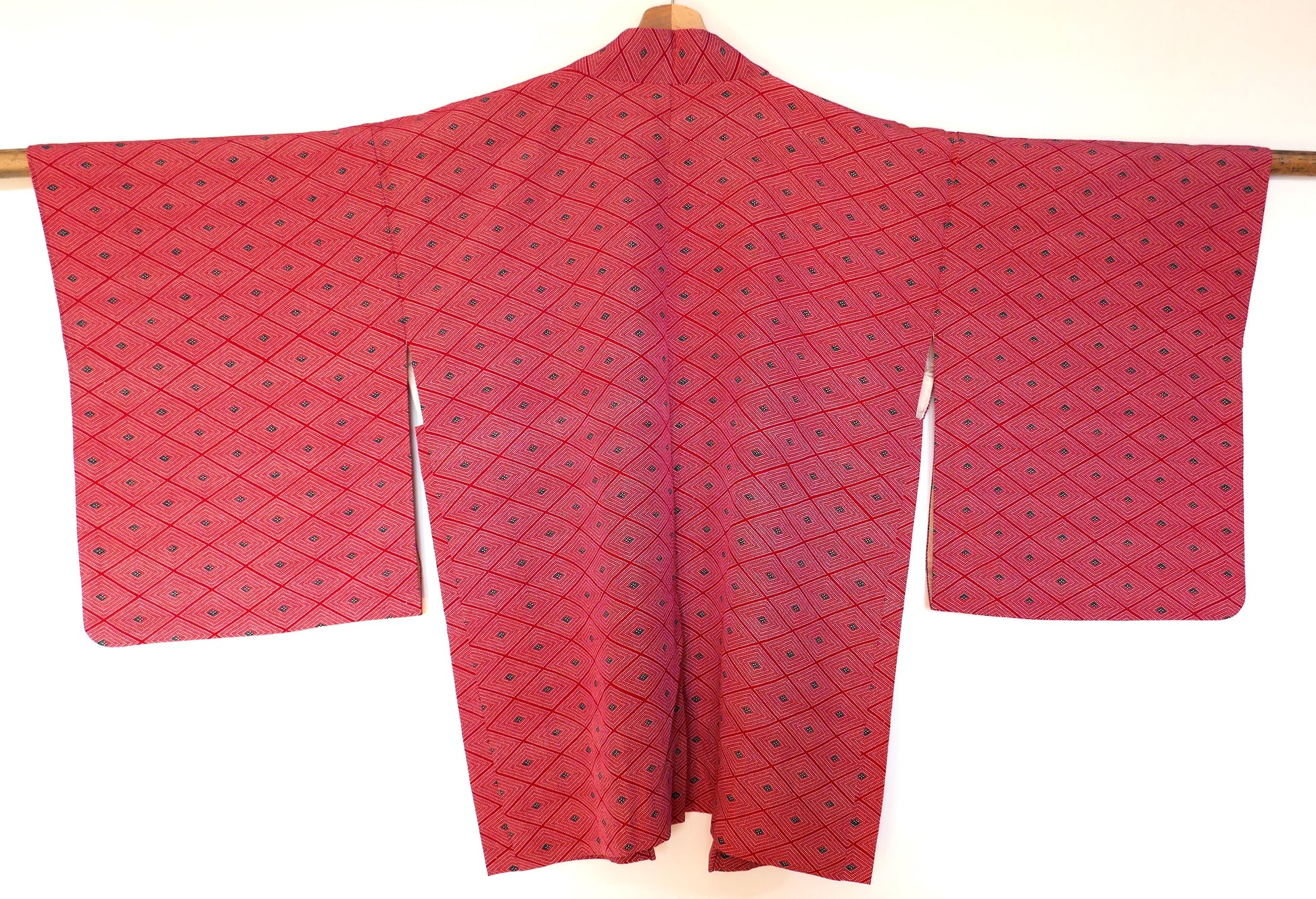  Vue de dos complète d’un haori vintage suspendu, en soie rouge à motifs géométriques losange (菱形).
