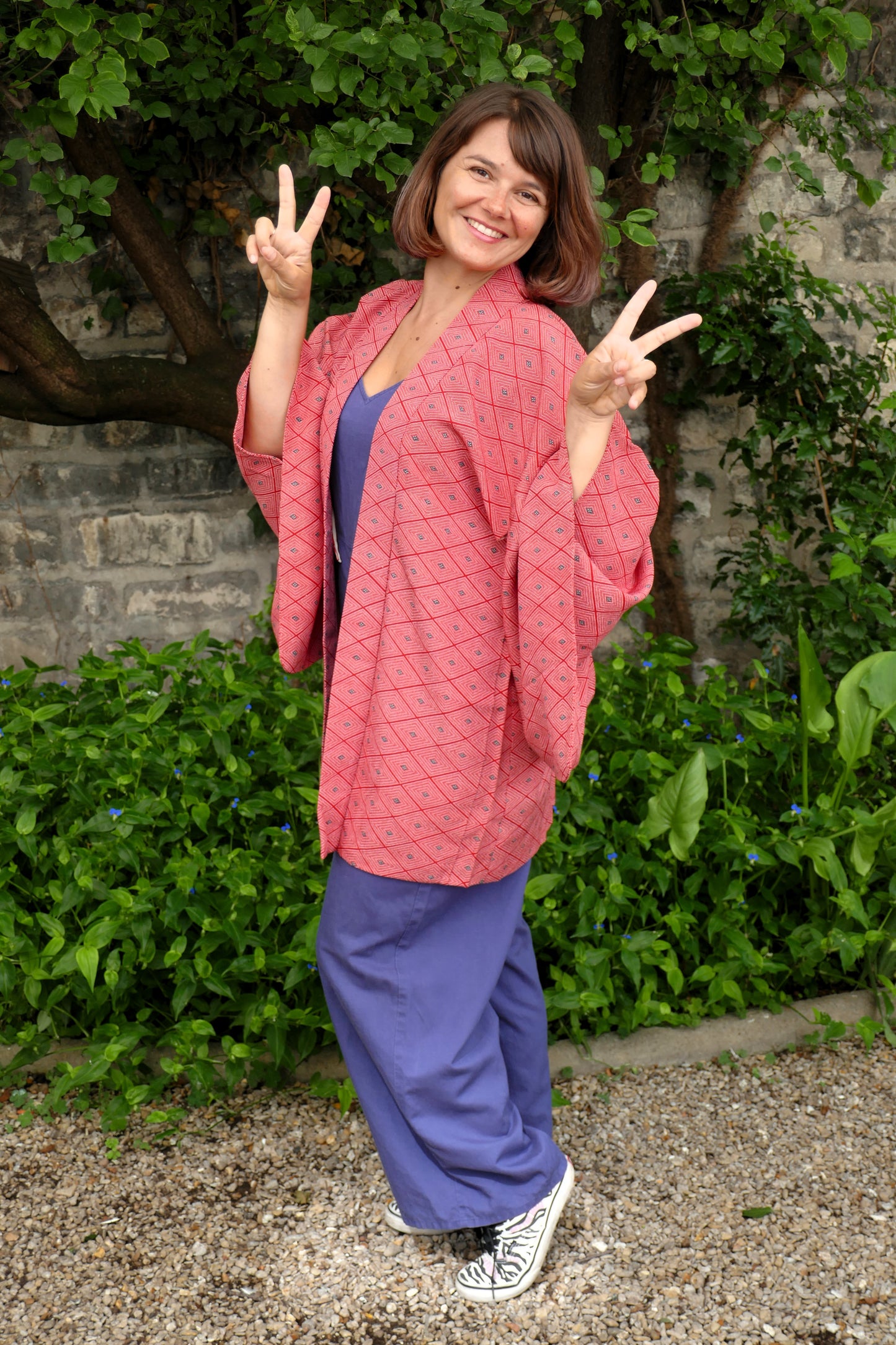 Femme souriante portant un haori vintage rouge à motifs losange, en extérieur de trois quarts