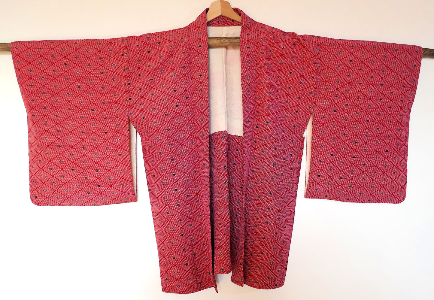 Haori vintage en soie rouge suspendu sur un cintre, montrant le motif géométrique en losanges et la coupe traditionnelle.