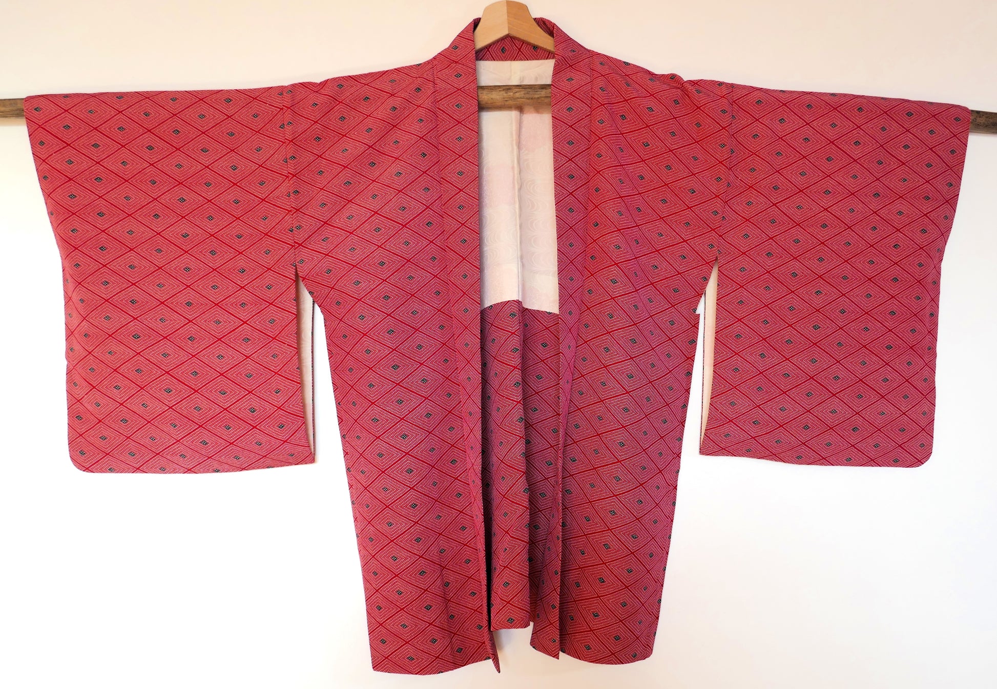 Haori vintage en soie rouge suspendu sur un cintre, montrant le motif géométrique en losanges et la coupe traditionnelle.