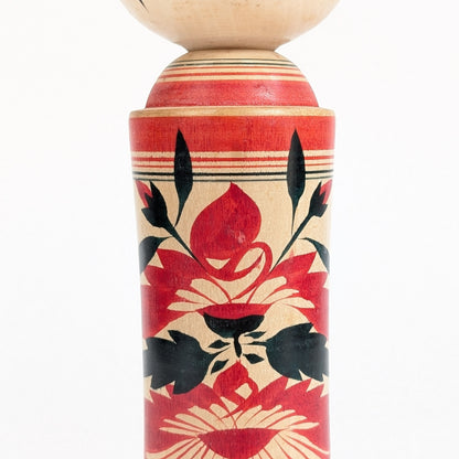 Gros plan du motif hishigiku 菱菊, chrysanthème emblématique peint en rouge et noir sur une kokeshi traditionnelle de Naruko.