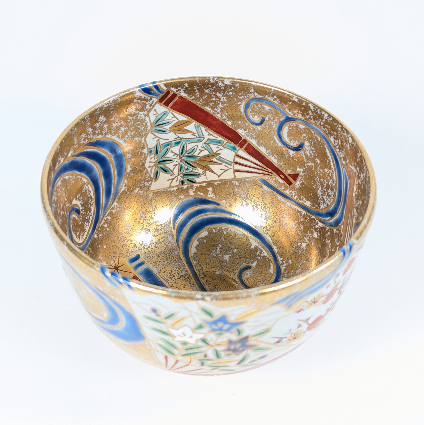 Intérieur du bol à matcha japonais avec éventail aux feuilles de bambou sasa, vagues bleues stylisées et fond doré moucheté.