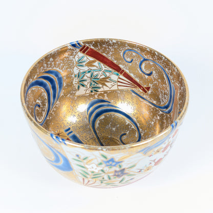 Intérieur du bol à matcha japonais avec éventail aux feuilles de bambou sasa, vagues bleues stylisées et fond doré moucheté.