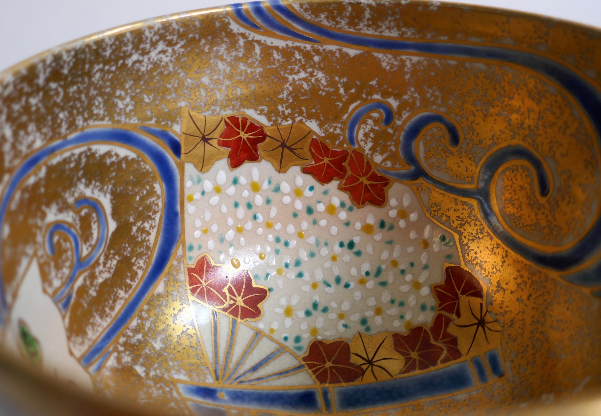 Détail intérieur du chawan avec éventail fleuri, feuilles d’érable momiji, motifs de vagues et fond doré en iro-e.