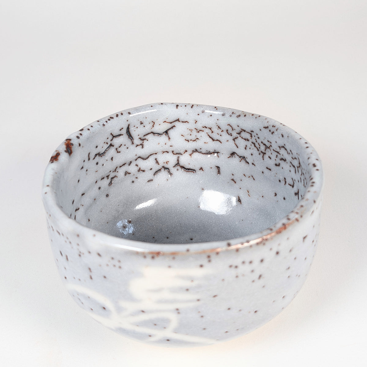 Intérieur du chawan Shino avec épaisse glaçure feldspathique gris bleuté, texture yuzuhada et ponctuations ferrugineuses.