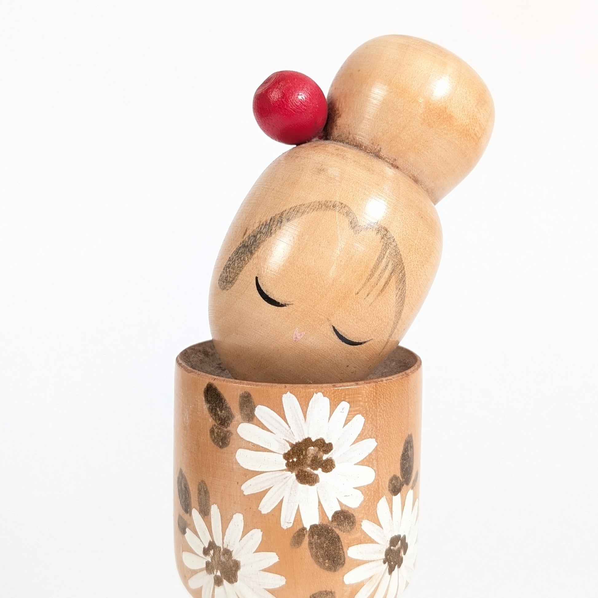 Détail du visage peint d’une kokeshi Ishida Tomio, yeux fermés, tête inclinée et chignon orné de rouge.