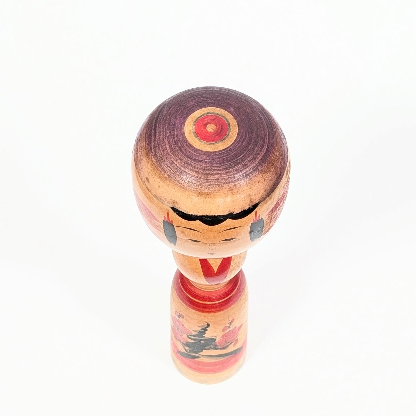 Vue du dessus d’une kokeshi Yajirō montrant le motif janome en cercles concentriques rouges et violets sur la tête