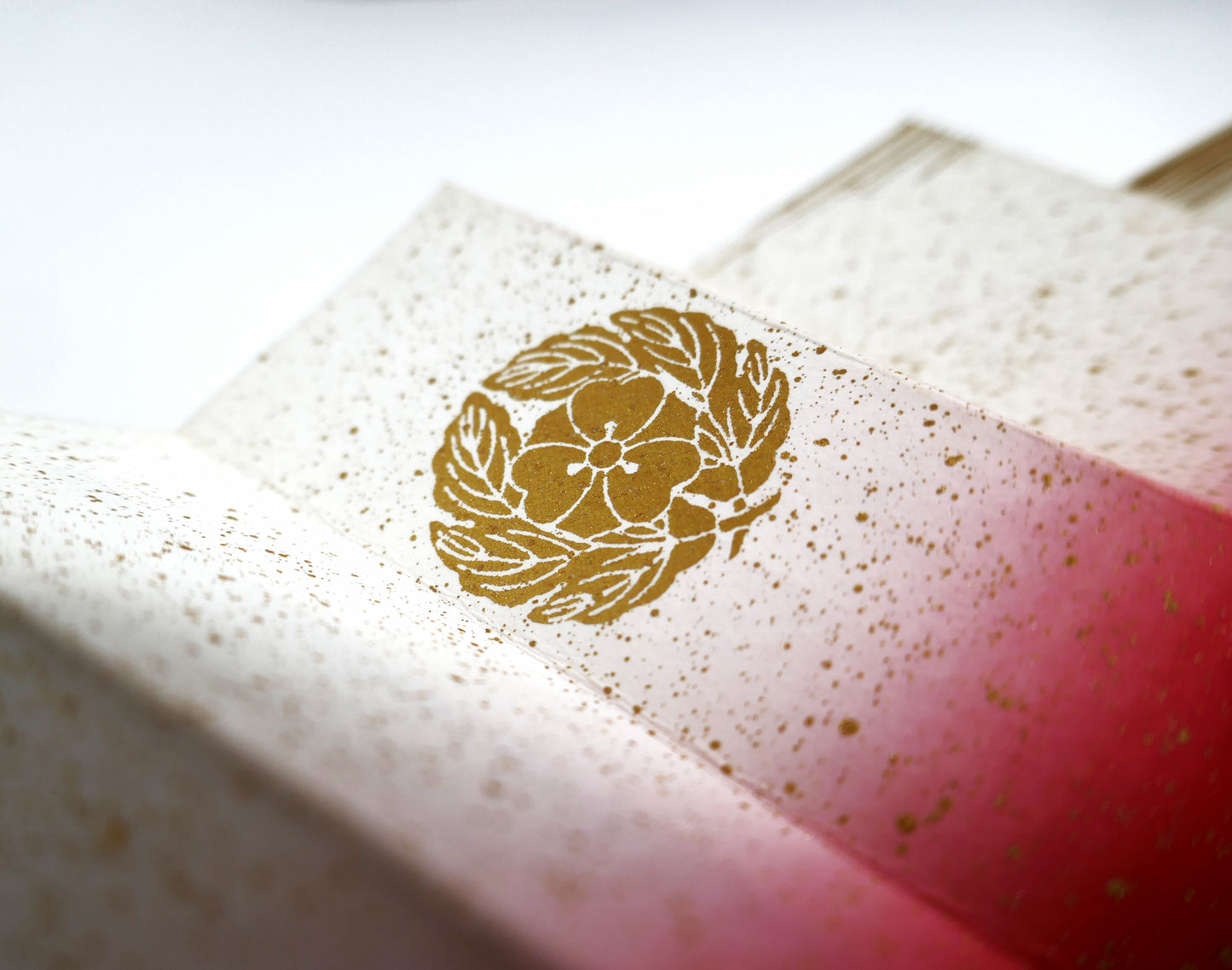 Gros plan sur un kamon doré imprimé sur un éventail japonais en papier épais, illustrant un blason floral inspiré des motifs de l’époque Shōwa.