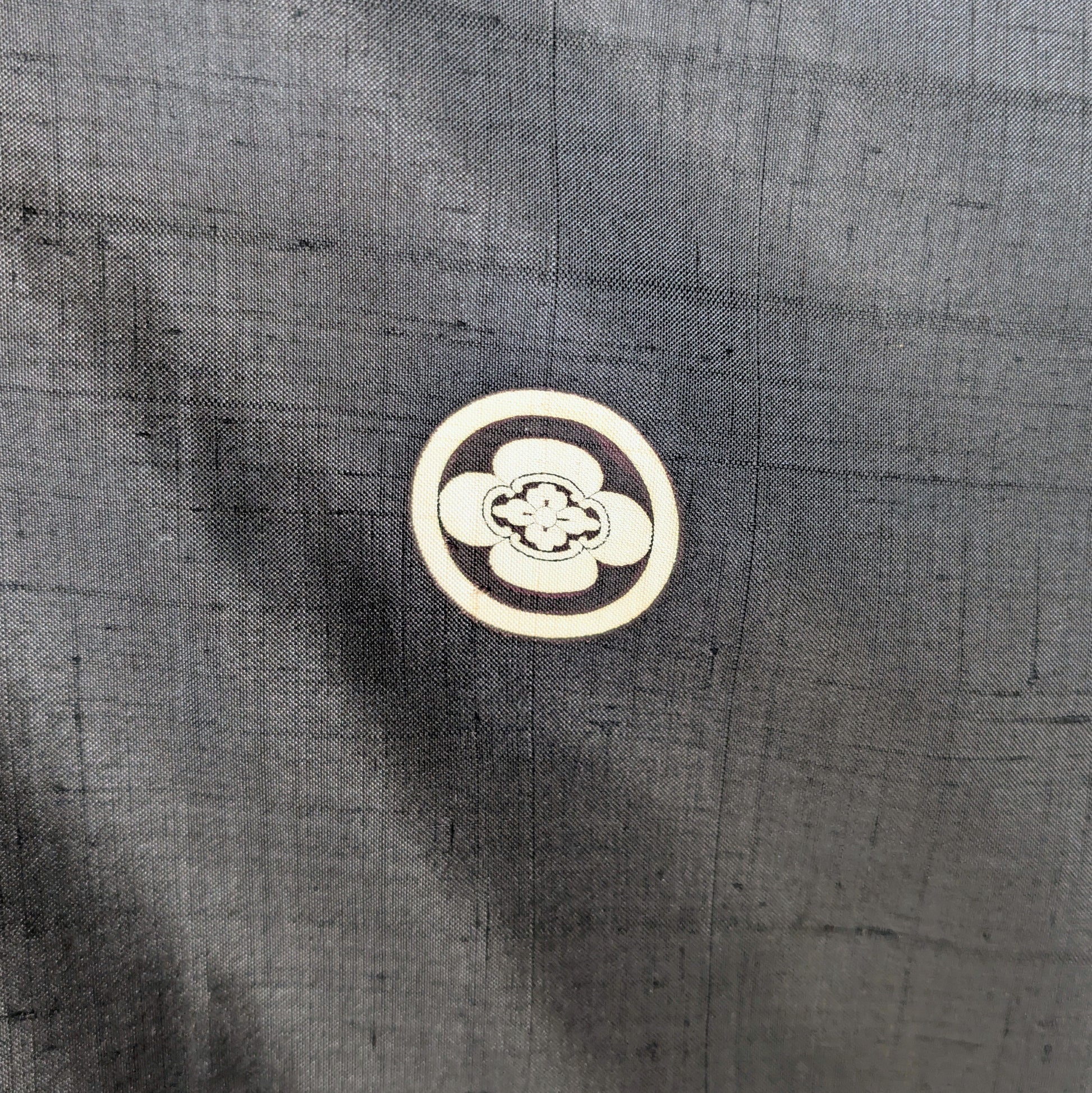 Gros plan sur le kamon japonais Maru Mokkō, emblème familial appliqué sur un haori en soie noire