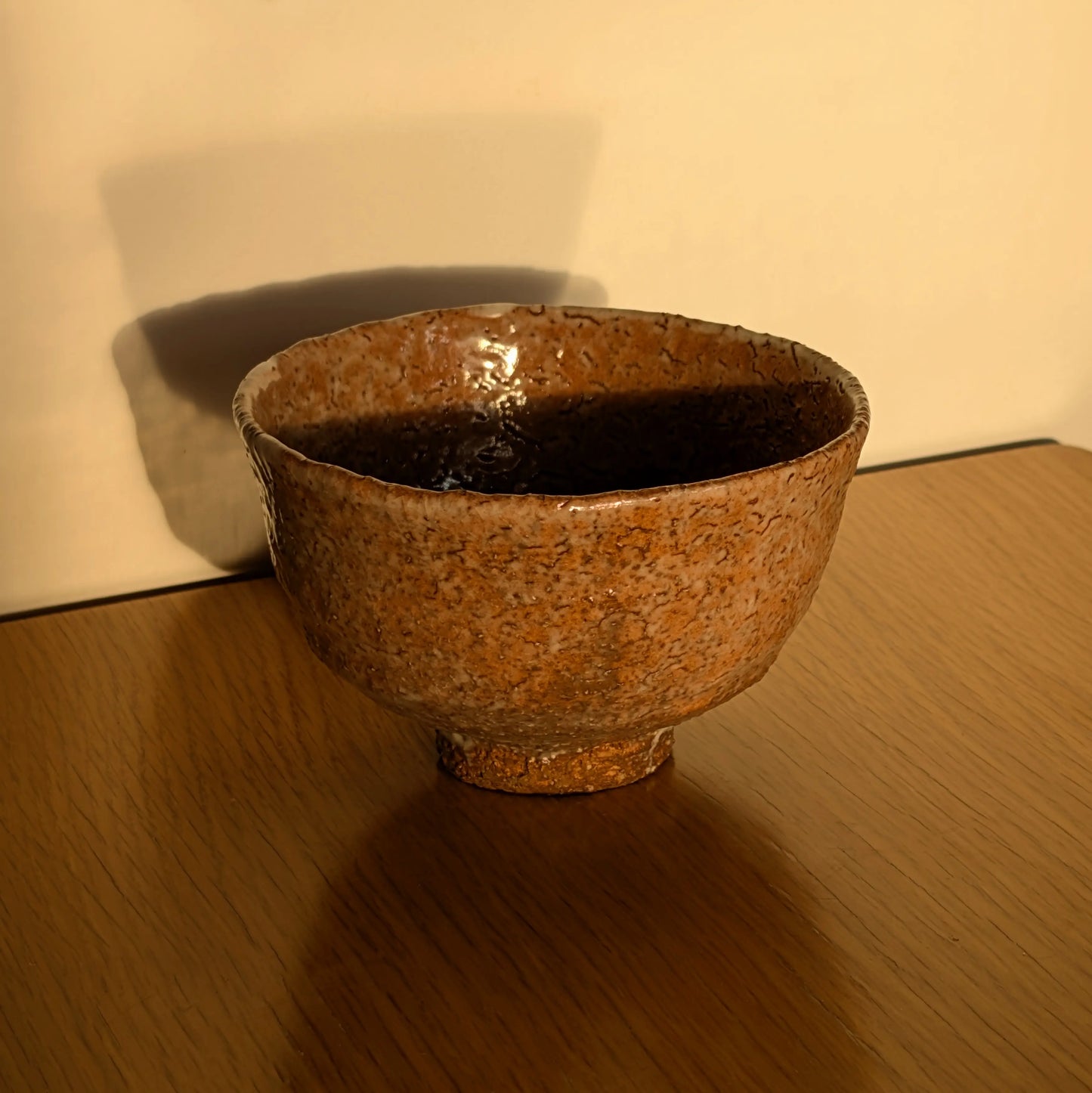 Chawan Iwakuni-yaki de Yamada Shōtō éclairé par une lumière chaude, glaçure texturée et silhouette évasée sur table en bois