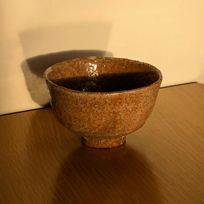 Chawan Iwakuni-yaki de Yamada Shōtō éclairé par une lumière chaude, glaçure texturée et silhouette évasée sur table en bois