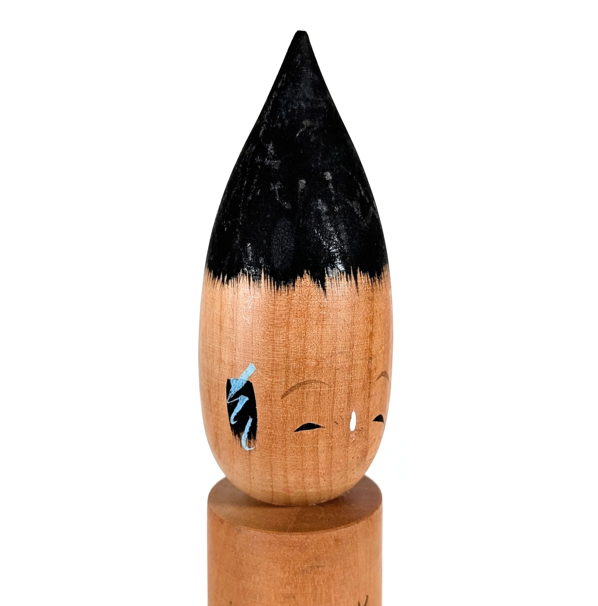 Gros plan du visage : kokeshi fude en bois, expression sereine, détails peints (yeux, sourcils, mèches bleutées), objet japonais vintage.