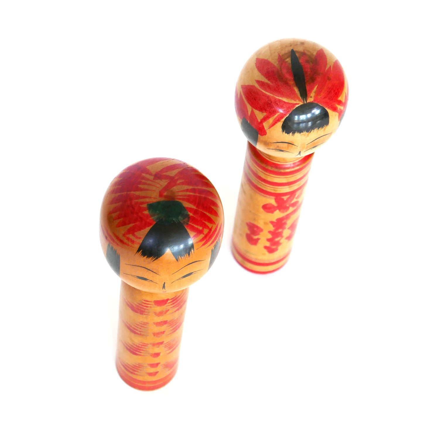 Vue de dessus de deux kokeshi japonaises artisanales, à motifs floraux rouges peints sur la tête.