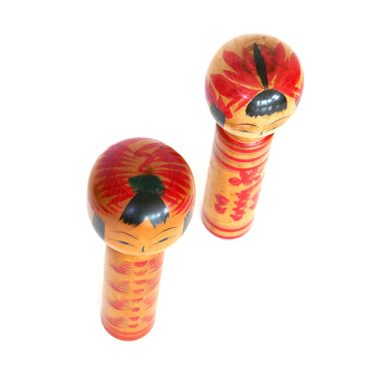 Vue de dessus de deux kokeshi japonaises artisanales, à motifs floraux rouges peints sur la tête.