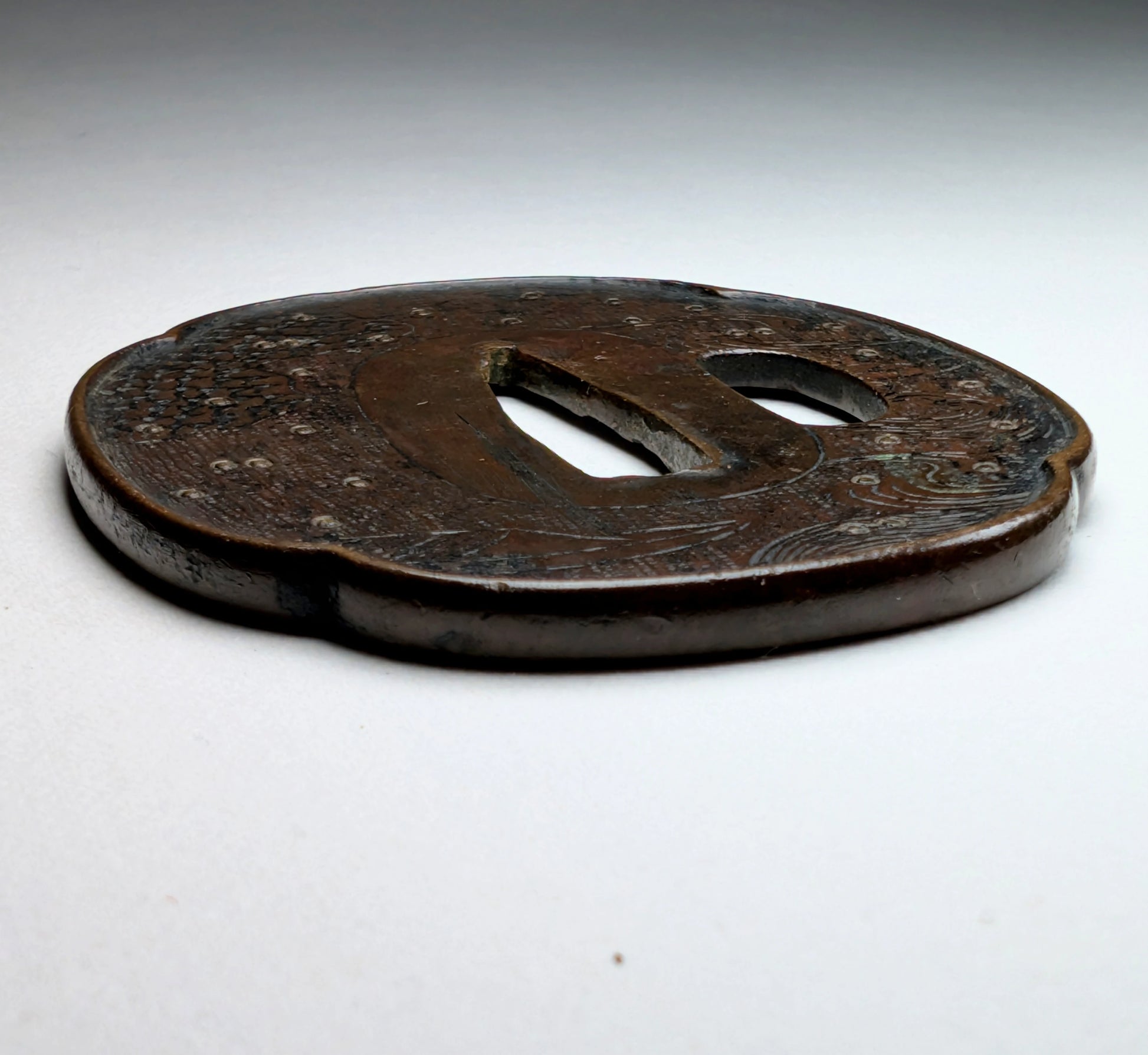 Tsuba japonaise Edo tardif en fer forgé, vue en angle rasant, style Shoami, décor gravé de vagues et bateau, fitting de wakizashi.
