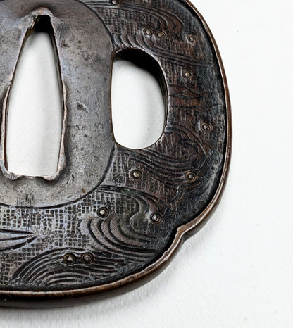 Détail d’une tsuba de wakizashi Edo Shoami, motif maritime avec vagues profondes et bateau stylisé.